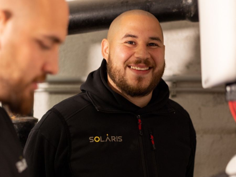 Zwei Solaris-Elektriker bei der Arbeit im Technikraum, einer lächelt in die Kamera